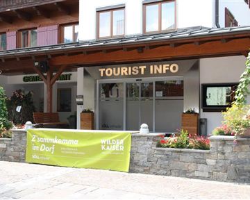 Ein Gebäude mit dem Schild "TOURIST INFO" an der Fassade. Vor dem Eingang stehen Blumen und Pflanzen in Töpfen.
