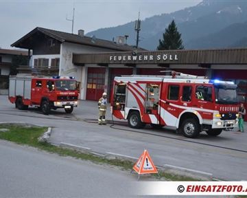Zwei Feuerwehrfahrzeuge stehen vor der Feuerwehrstation in Söll. Im Hintergrund sind Berge und eine ländliche Umgebung zu sehen.