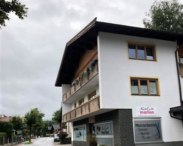A two-story building with a hair salon and a clear street layout. Flowers are above the entrance and the sky is cloudy.