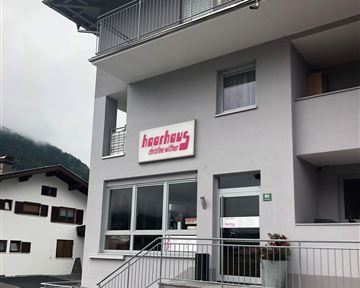 Ein modernes Gebäude mit einem klaren, minimalistischen Design. Vor dem Eingang steht ein Schild mit dem Namen „Haarhaus“.