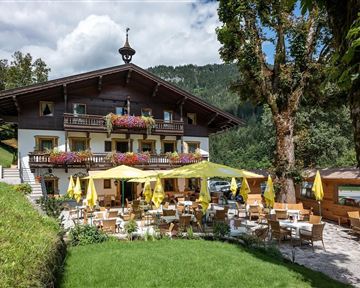 Ein gemütliches Restaurant in den Bergen mit einer einladenden Terrasse. Gelbe Sonnenschirme und Blumen schmücken die Außenbereiche.