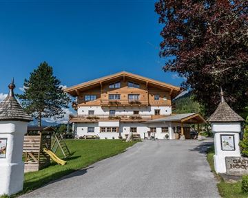 A picturesque Alpine house with wooden cladding and a beautiful garden. In the foreground, a paved driveway leads to the front door.