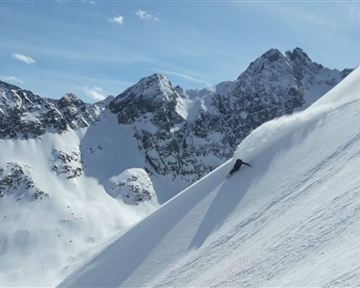 A beautiful winter mountain landscape with snow-covered peaks. A skier is skiing down the slope, leaving a trail in the fresh snow.