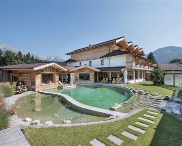 Ein modernes Haus mit Holzverkleidung und einem schönen Garten. Im Vordergrund befindet sich ein geschwungener Pool mit einer modernen Wasserlandschaft.