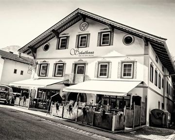 A traditional Bavarian inn with a distinctive architectural style. The facade is in black and white, and there is a terrace with outdoor seating.