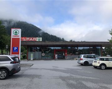 A SPAR store in a rural setting, surrounded by mountains and trees. In front of the shop is a parking lot with several cars.