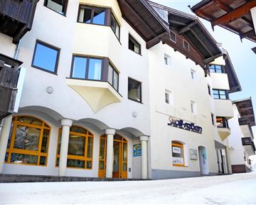 A modern building with a bright facade and large windows. The lower floors have storefronts with bright frames, and the street is paved.