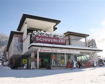 A modern ski rental shop in a snowy winter landscape. The facade features large windows and an inviting sign that reads "Ski Rental".