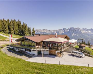 An alpine mountain hut with a beautiful view of the mountains. Surrounded by trees and green grass, it offers an inviting atmosphere.