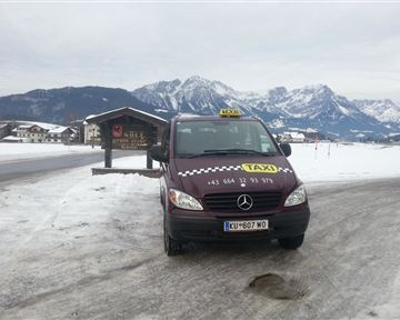 A taxi is standing on a snow-covered road with a picturesque mountain landscape in the background. The surroundings are wintry and tranquil.