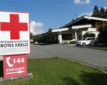 A building of the Austrian Red Cross in Söllandl. In the foreground is a large red cross sign with the phone number 144.