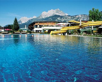 Ein glitzernder Pool mit einem gelben Wasserrutschen und einer schönen Berglandschaft im Hintergrund. Ein entspannender Ort, ideal für einen Tag am Wasser.