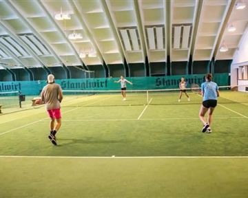 Ein Tennisplatz in einer Halle mit vier Spielern. Die Atmosphäre ist aktiv und konzentriert.