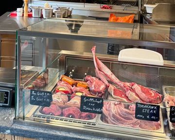 A meat stand with various types of meat behind a glass display. Clearly visible price tags indicate the products.