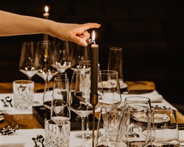 An elegant dining table with glasses and cutlery. A hand lights a candle, creating a cozy atmosphere.