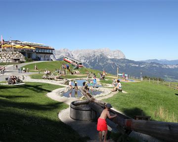 Ein schöner Bergbereich mit Spielmöglichkeiten für Kinder. Im Hintergrund ist eine beeindruckende Berglandschaft zu sehen.