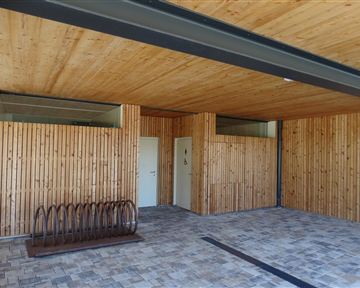 Ein moderner Raum mit Holzverkleidung und einer hellen Decke. Links befindet sich ein Fahrradständer und zwei Türen.