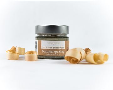 Ein Glas mit Natur-Salzpeeling steht auf einem weißen Hintergrund. Daneben liegen einige Holzspäne.