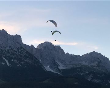 Zwei Gleitschirme fliegen über majestätische Berge. Der Himmel ist klar und zeigt die Schönheit der Natur.
