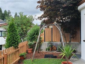 Ein schöner Garten mit einem Holzschaukel, grünen Pflanzen und einem Holzzaun. Der Himmel ist bewölkt und die Atmosphäre ist ruhig.