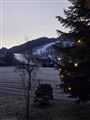 A wintry morning with snow-covered hills and a village in the background. A Christmas tree with lights stands in the foreground.