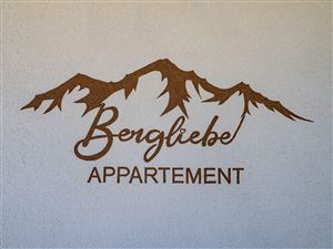 Ein dekoratives Schild mit der Aufschrift "Bergliebe Appartement" über stilisierten Bergen. Das Design vermittelt eine gemütliche und einladende Atmosphäre.