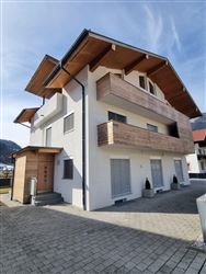 Ein modernes Haus mit einem klaren, weißen Fassaden und Holzbalkonen. Die Architektur ist schlicht und ansprechend, umgeben von einem gepflasterten Bereich.