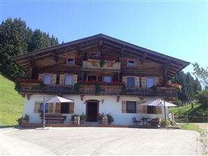 Ein traditionelles Chalet mit einer Holzfassade und Blumen auf dem Balkon. Im Vordergrund befinden sich Tische und Sonnenschirme.