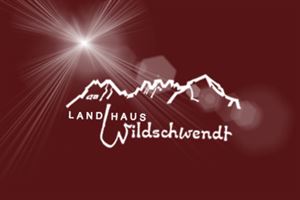 Ein stilisiertes Logo mit dem Schriftzug "Landhaus Wildschwendt" und einer Bergsilhouette im Hintergrund. Die Farben sind rot und weiß, mit einer Lichtstrahlen-Element.