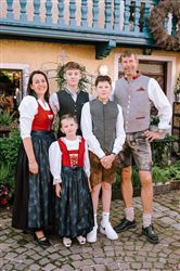Eine Familie in traditioneller bayerischer Tracht steht zusammen. Sie lächeln vor einem dekorierten Hintergrund.