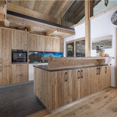 Eine moderne Küche aus Holz mit stilvollen Möbeln und einem geräumigen Layout. Große Fenster lassen viel Licht herein und bieten einen Blick auf die Umgebung.