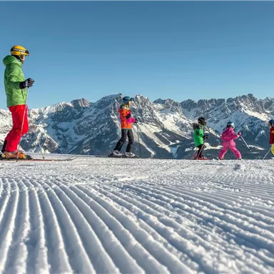 A group of skiers enjoys a sunny day on a snow-covered slope. In the background, impressive mountains can be seen.