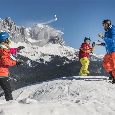 A cheerful family is playing in the snow on a mountain. They are wearing colorful winter jackets and laughing as they throw snowballs at each other.