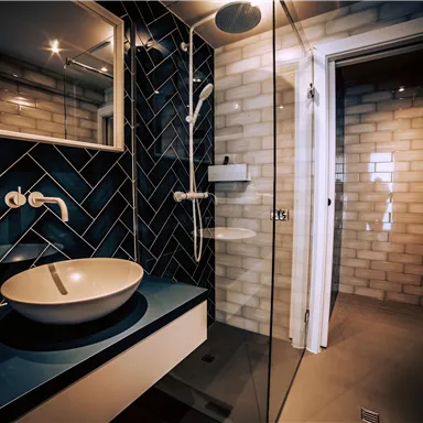 A modern bathroom with blue tiles and an elegant washbasin. The shower is open and the space is well-lit.