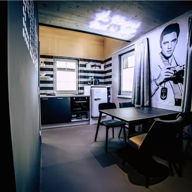 A modern kitchen with a dining table and chairs. A large picture of a person with a camera hangs on the wall.