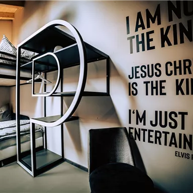 A modern room with a colorful loft bed and a cozy armchair. On the wall is a quote from Elvis Presley.