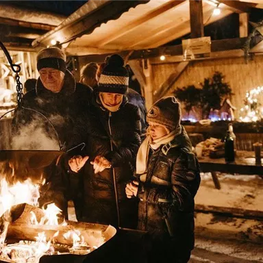 A cozy winter night with people gathered around a fire. The surroundings are festively lit, creating a warm atmosphere.