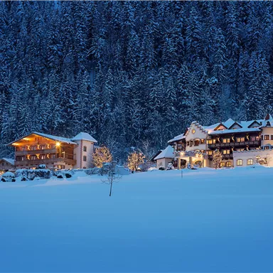 A wintry landscape with snow-covered hills. Cozy houses gently glow in the twilight.