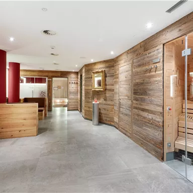 A modern wellness area with natural wooden walls and plain tiles. In the background, a sauna can be seen.