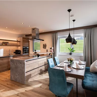 Modern kitchen with wooden shelves and a dining area. The space is bright and friendly with plants and elegant furniture.