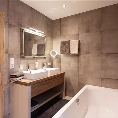 A modern bathroom with an elegant sink and a large mirror. The walls have a gray concrete look, and there is a freestanding bathtub.