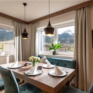 A modern dining room with a wooden table and elegant chairs. Large windows provide a view of the mountains and plenty of daylight.