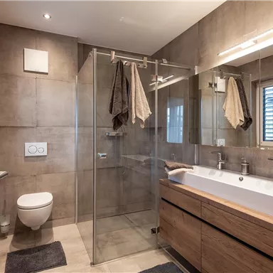 A modern bathroom with a glass shower and wooden shelves. The room is simply and elegantly designed.