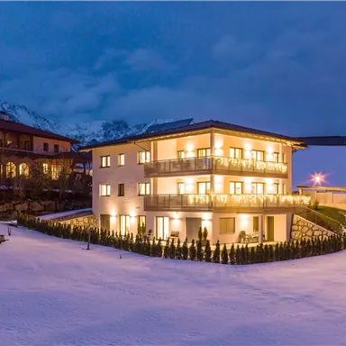 A modern building in the snow, surrounded by mountains. The warm lights illuminate the facade at dusk.