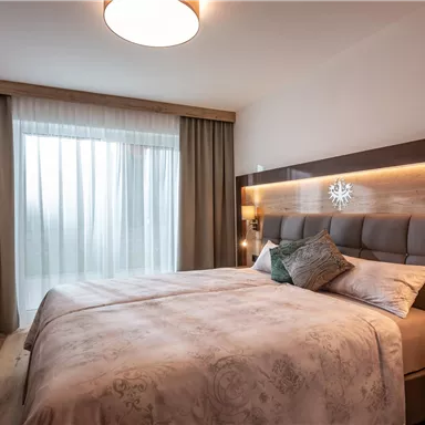 A cozy bedroom with a large bed and soft lighting. The curtains let in plenty of daylight and create a relaxed atmosphere.