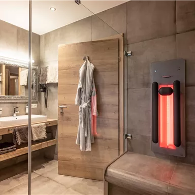 A modern bathroom with wood and concrete elements. There is a sink, a mirror, and an infrared heat lamp.