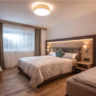 A modern hotel room with two beds and soft blankets. Large windows provide plenty of light and a pleasant atmosphere.