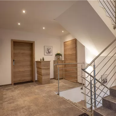 A modern entrance area with bright walls and a staircase. The floor is made of a simple material and there is stylish wooden furniture.