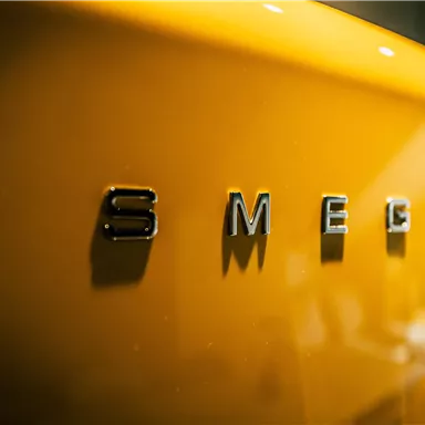 A yellow refrigerator with the brand "SMEG". The glossy surface reflects the light and creates a modern look.