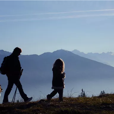A person, a child, and a dog are hiking in the mountains. The sky is clear and the landscape is surrounded by mountains.